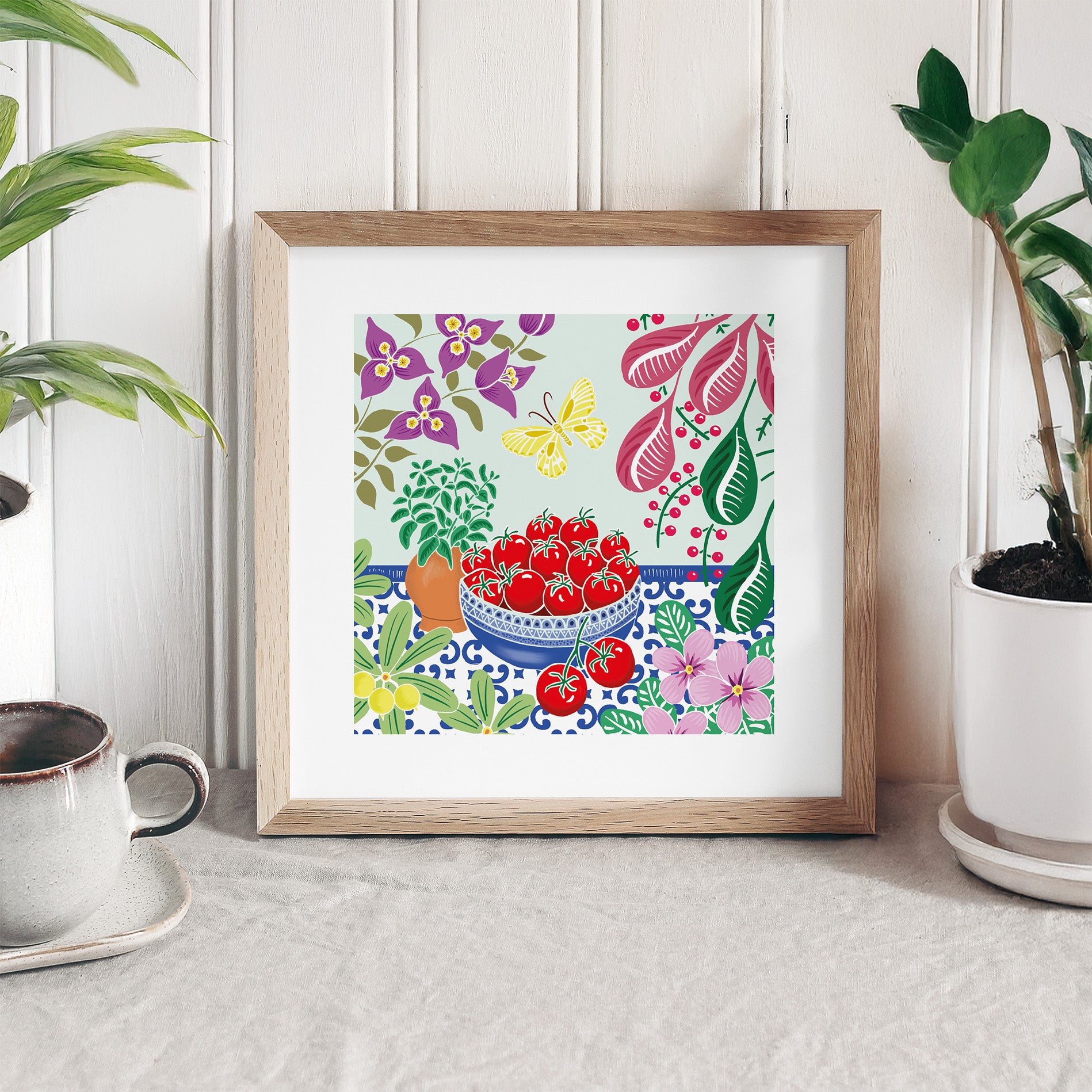 Framed artwork with a colorful design of tomatoes and flowers on a white surface.