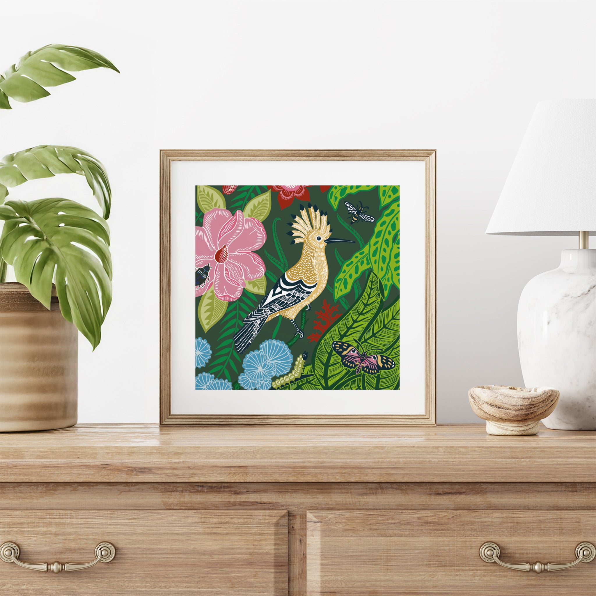 Framed artwork of a bird and flowers on a wooden surface with decorative items.