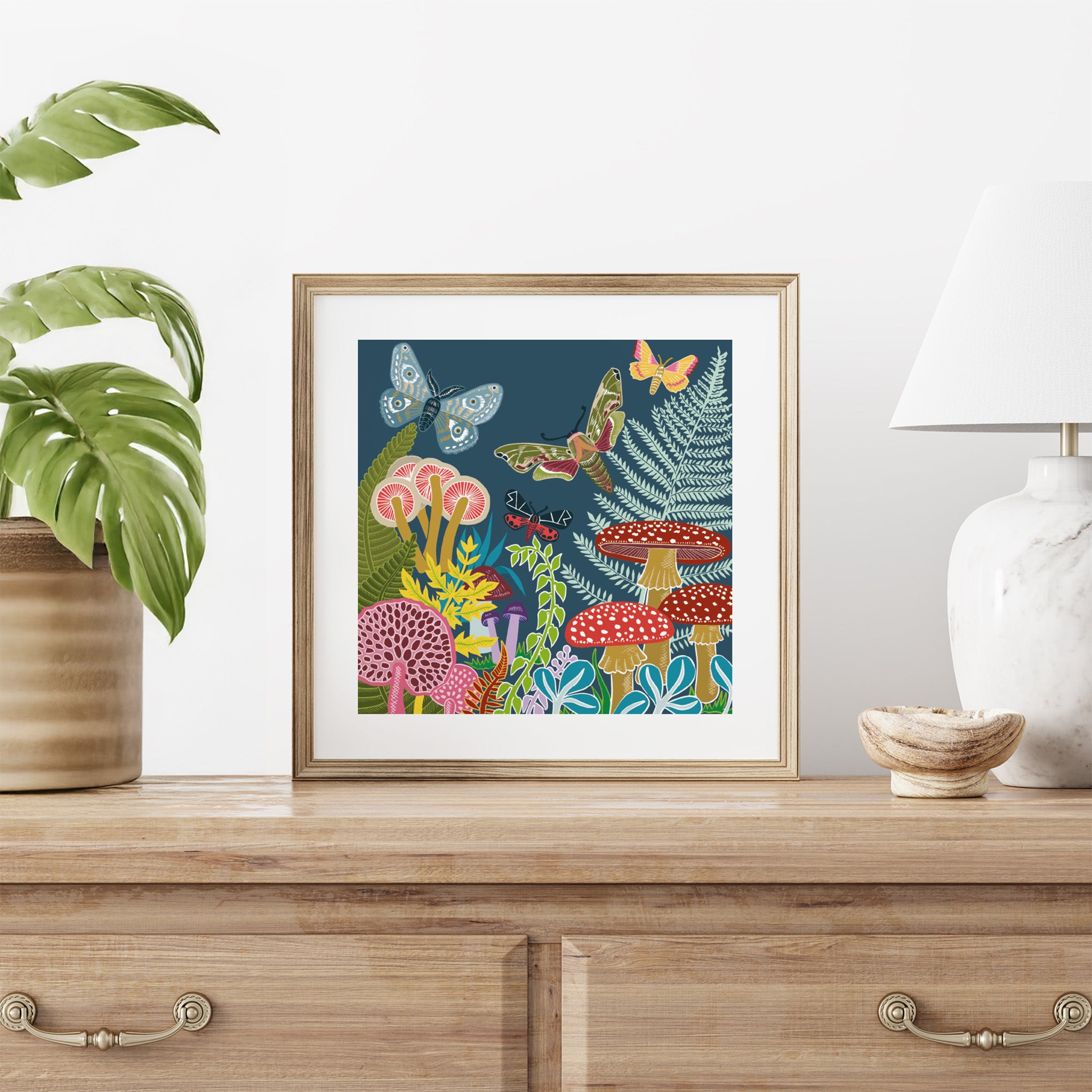 Framed artwork with mushrooms and butterflies on a wooden surface with decor items.