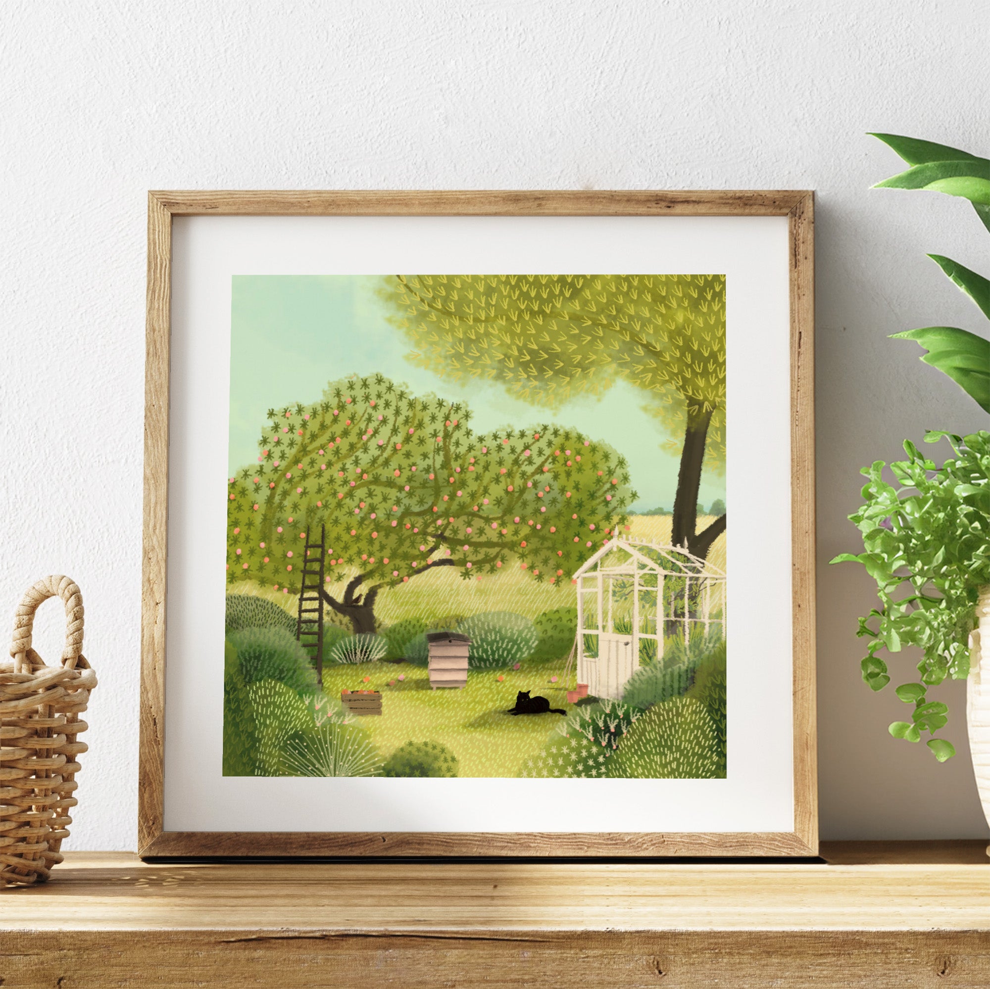 Framed artwork of a garden scene with trees and a greenhouse and a black cat, on a wooden shelf.