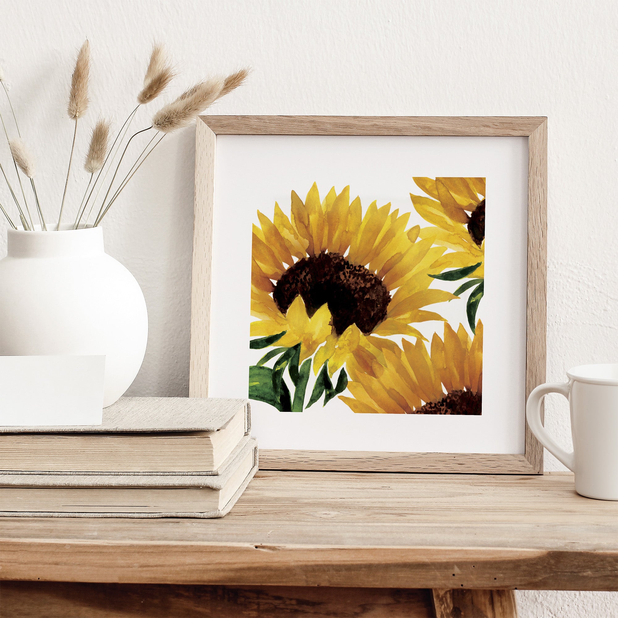 Framed artwork of sunflowers on a wooden surface with a vase and books in the background.