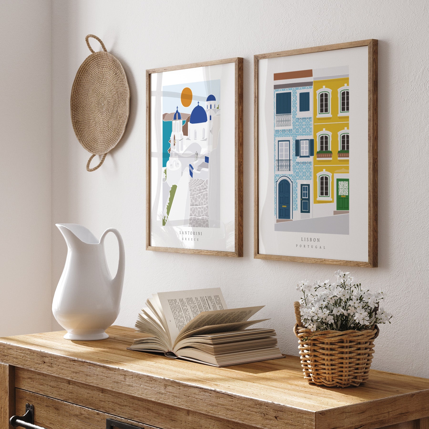 Decorative setup with framed artworks, a white pitcher, open book, and basket on a wooden surface.