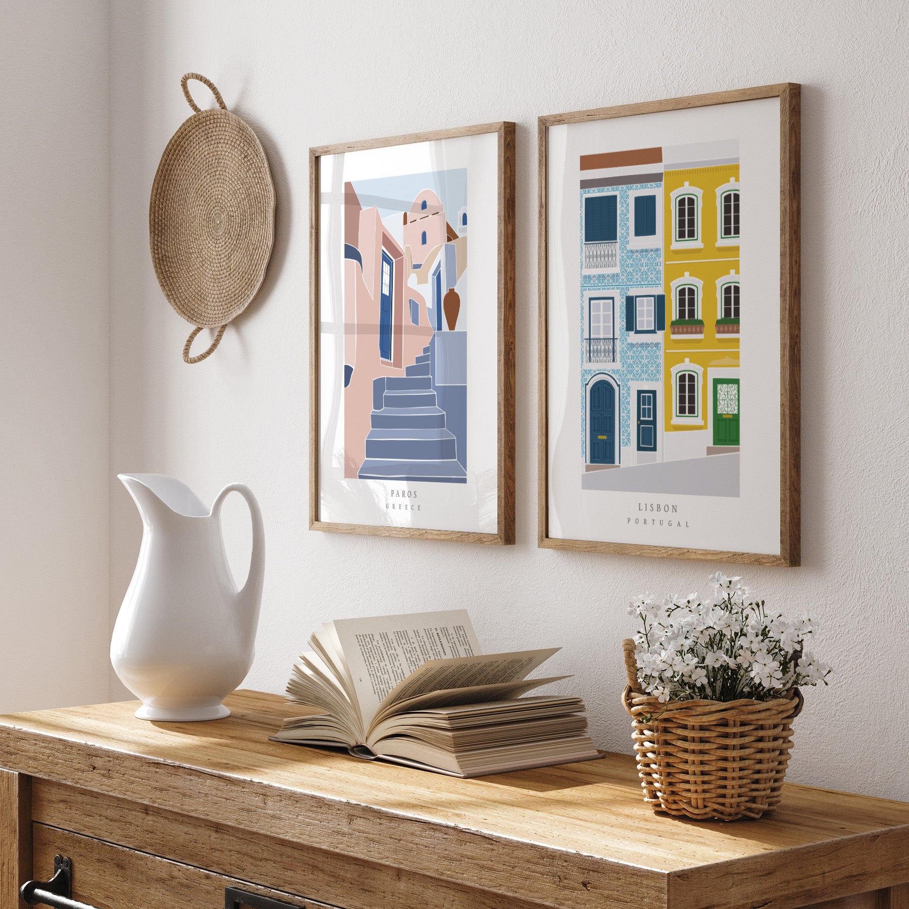 Decorative setup with framed artworks, a white pitcher, open book, and basket on a wooden surface.