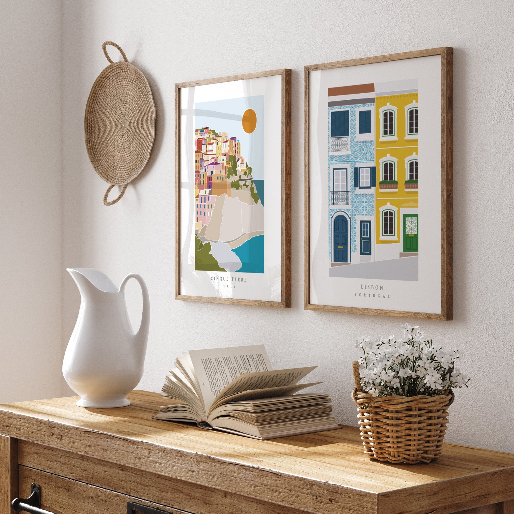 Decorative setup with framed artworks, a white pitcher, open book, and basket on a wooden surface.