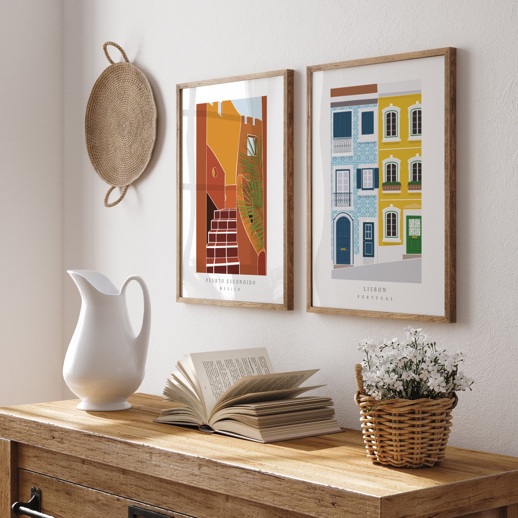 Decorative setup with framed artworks, a white pitcher, open book, and basket on a wooden surface.