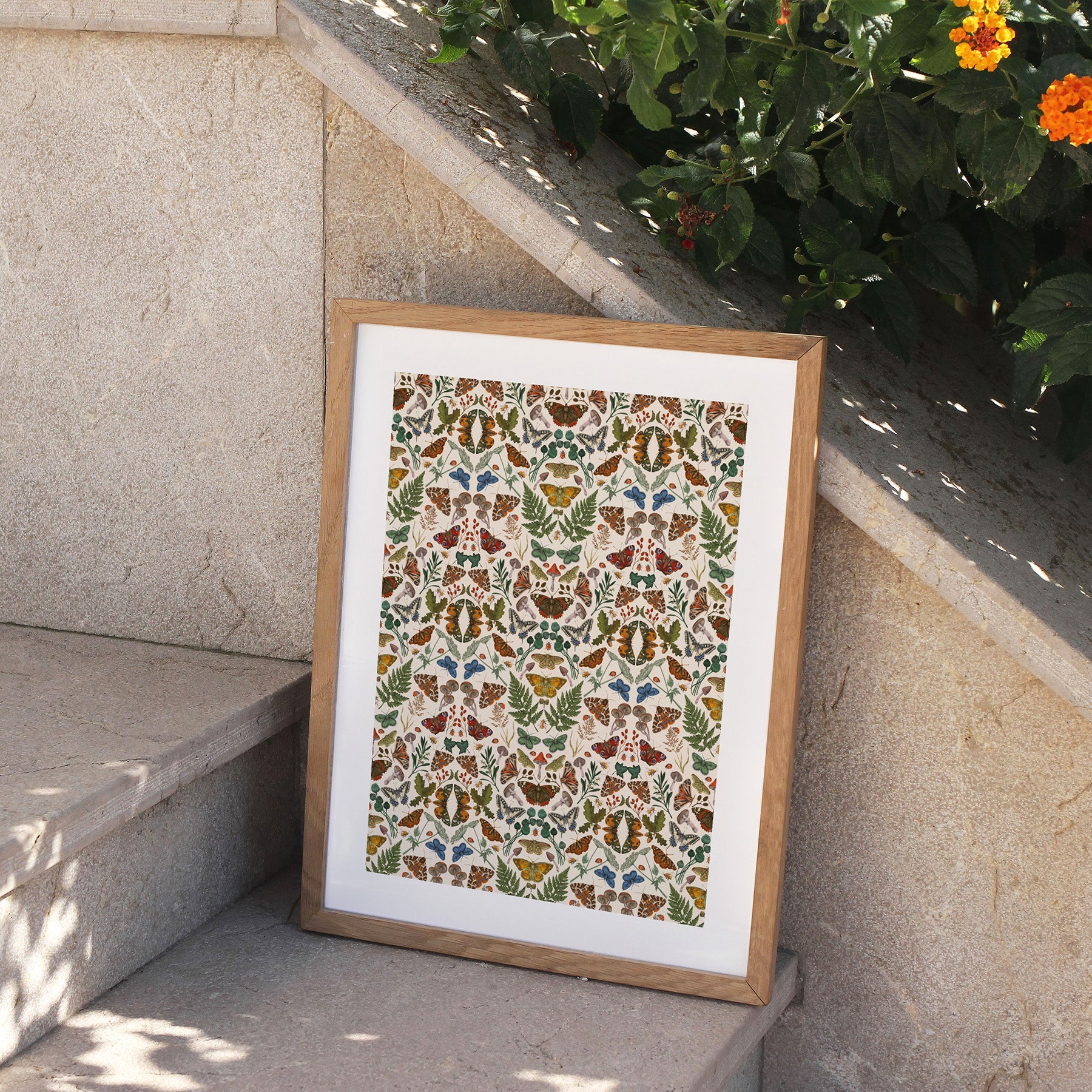 Framed floral pattern print on a stone surface with plants in the background.