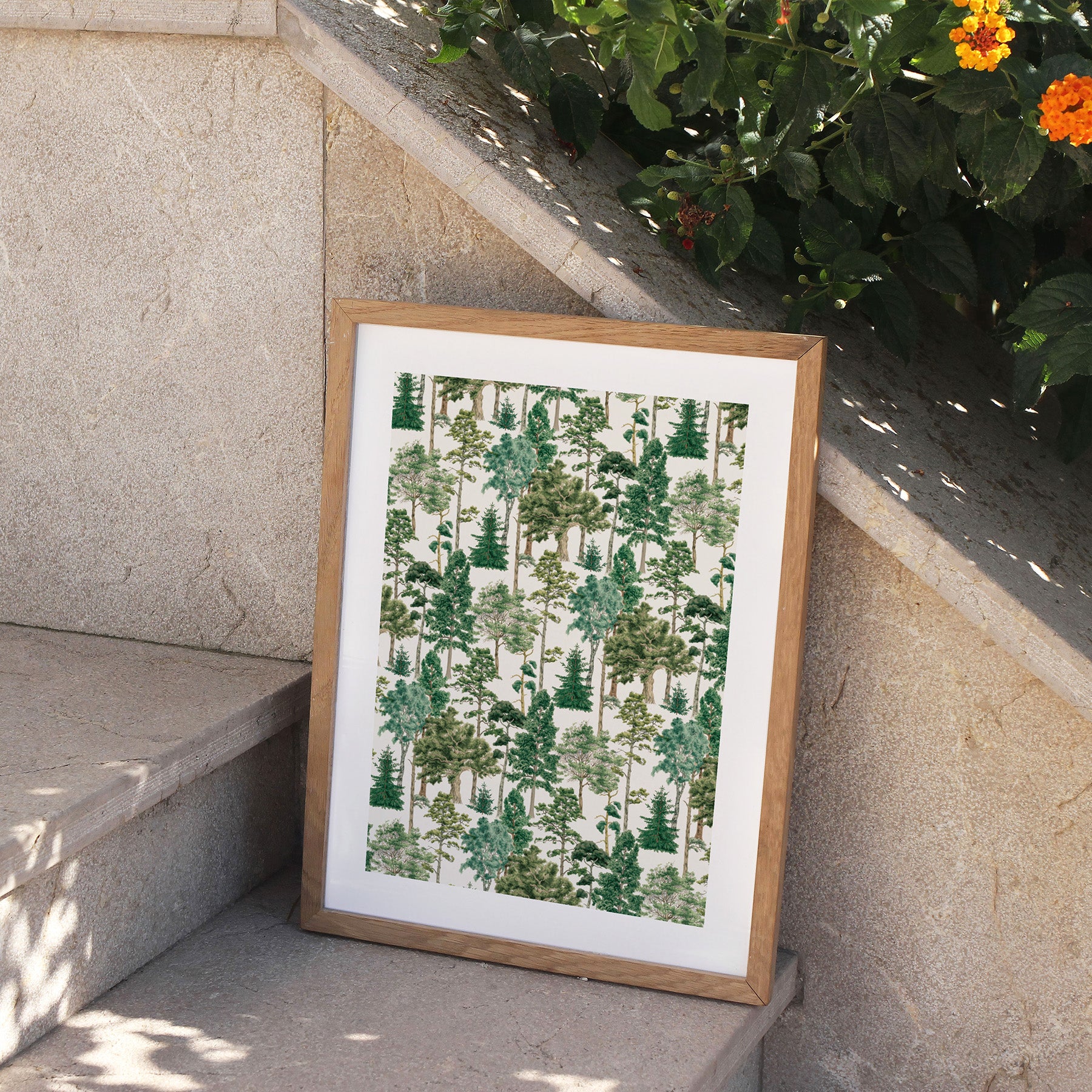 Framed forest pattern print on a stone ledge with plants in the background.