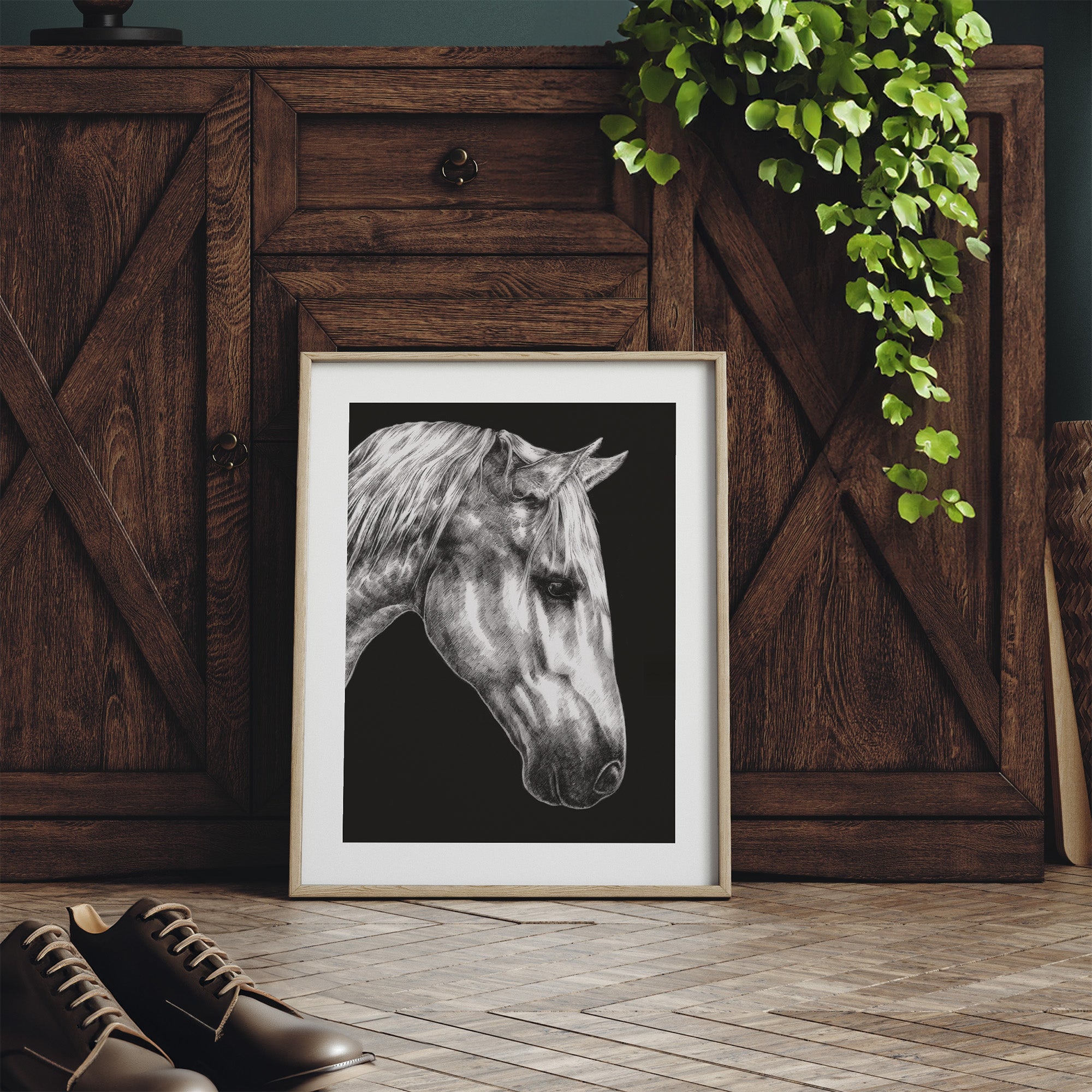 Framed black and white horse portrait on a wooden floor with a wooden cabinet and plant in the background.