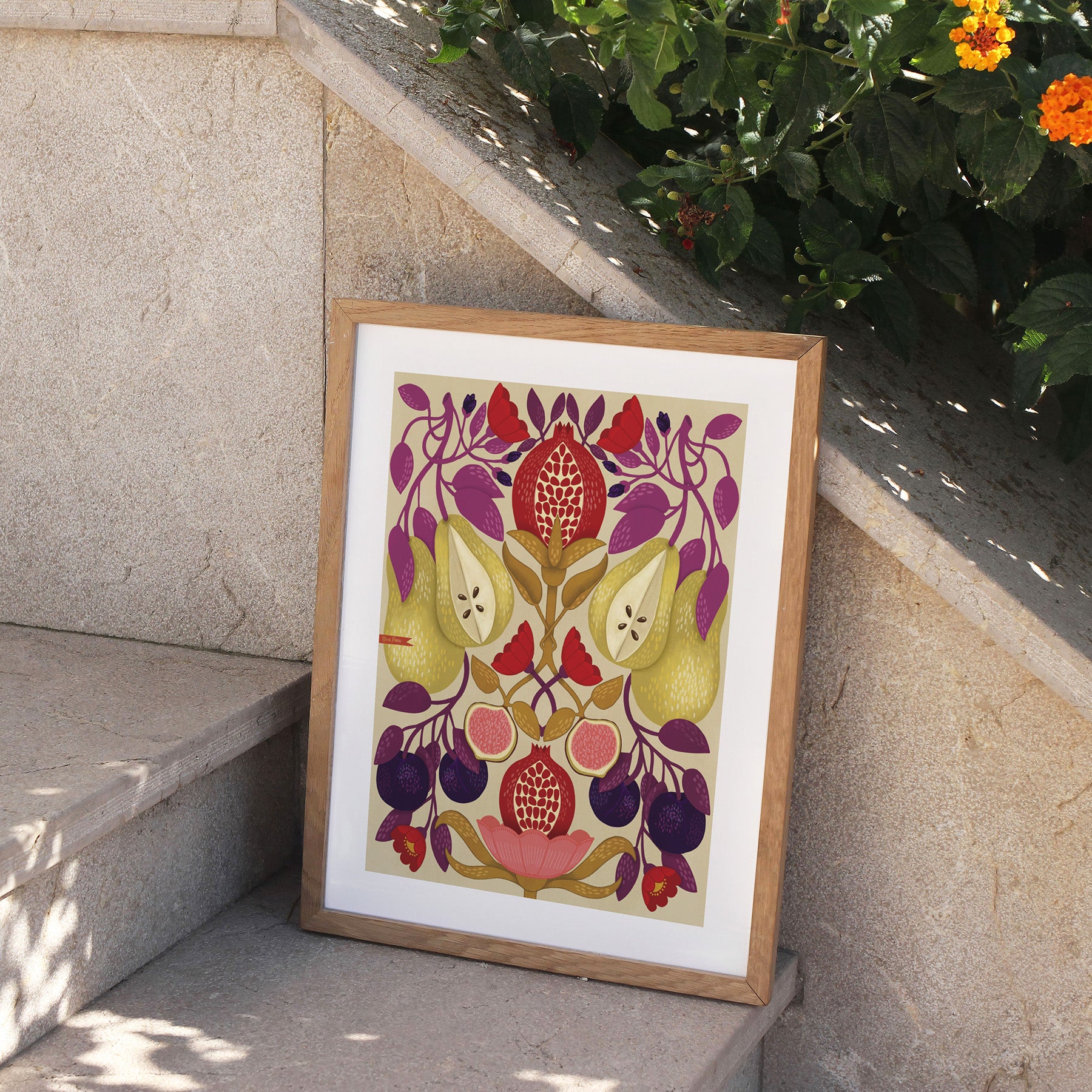 Framed artwork with floral design on a stone ledge with plants in the background.