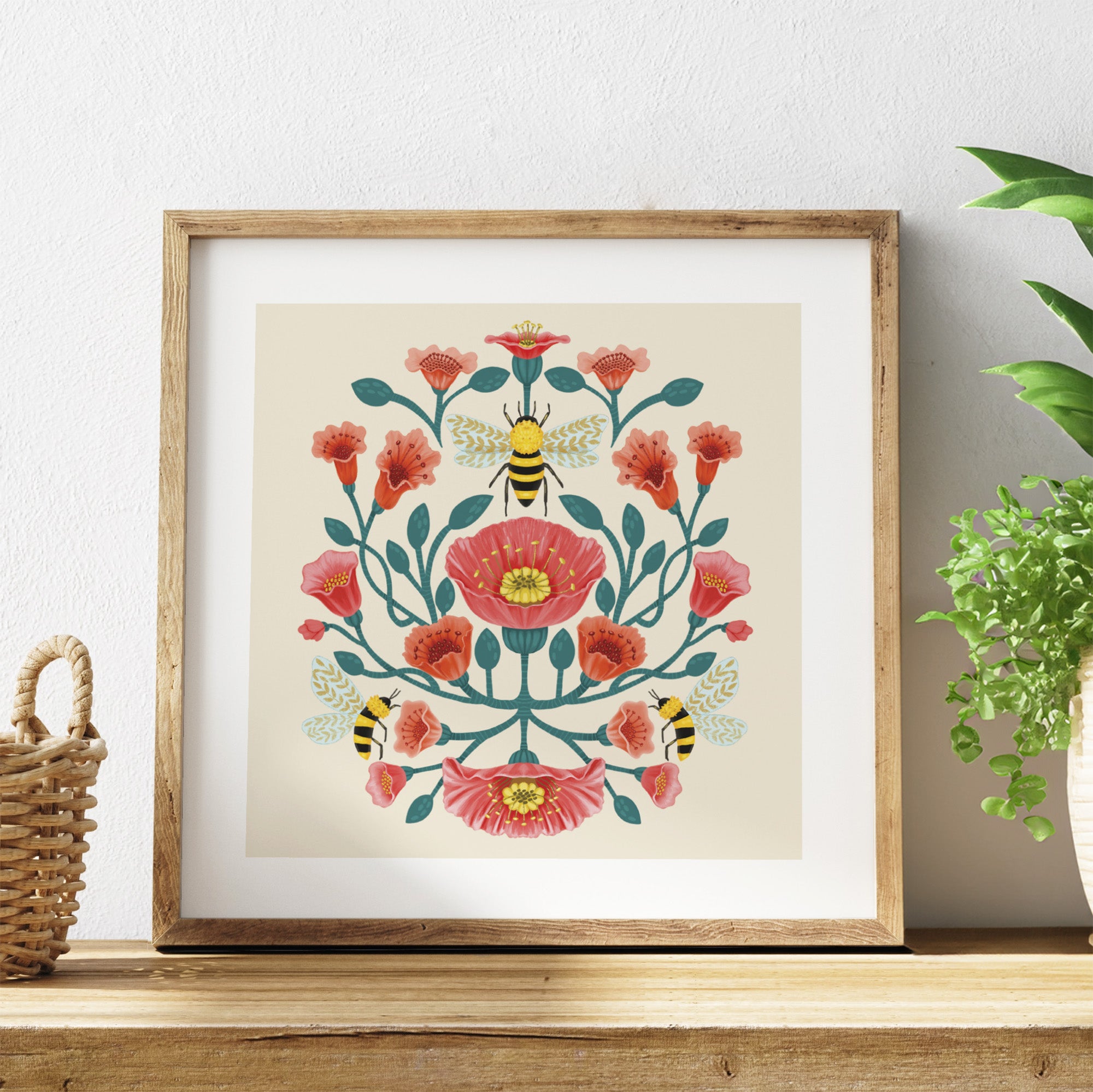 Framed artwork with floral design and bees on a shelf with a plant in the background.
