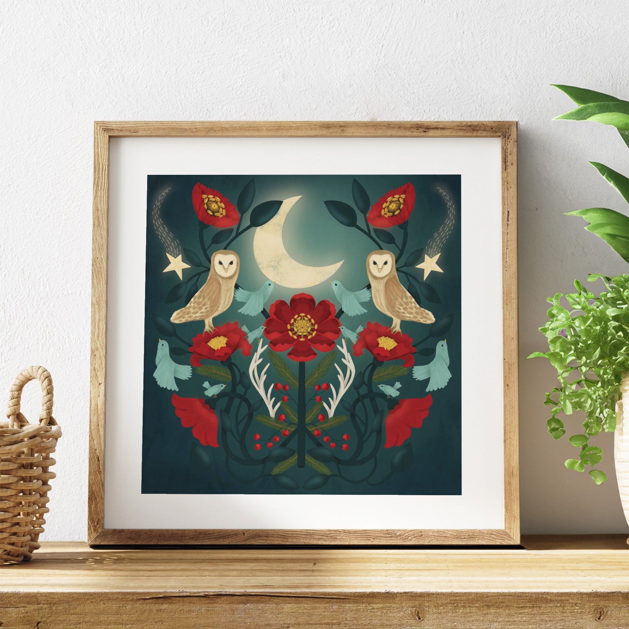 Framed artwork with owls, flowers, and a moon on a white wall.