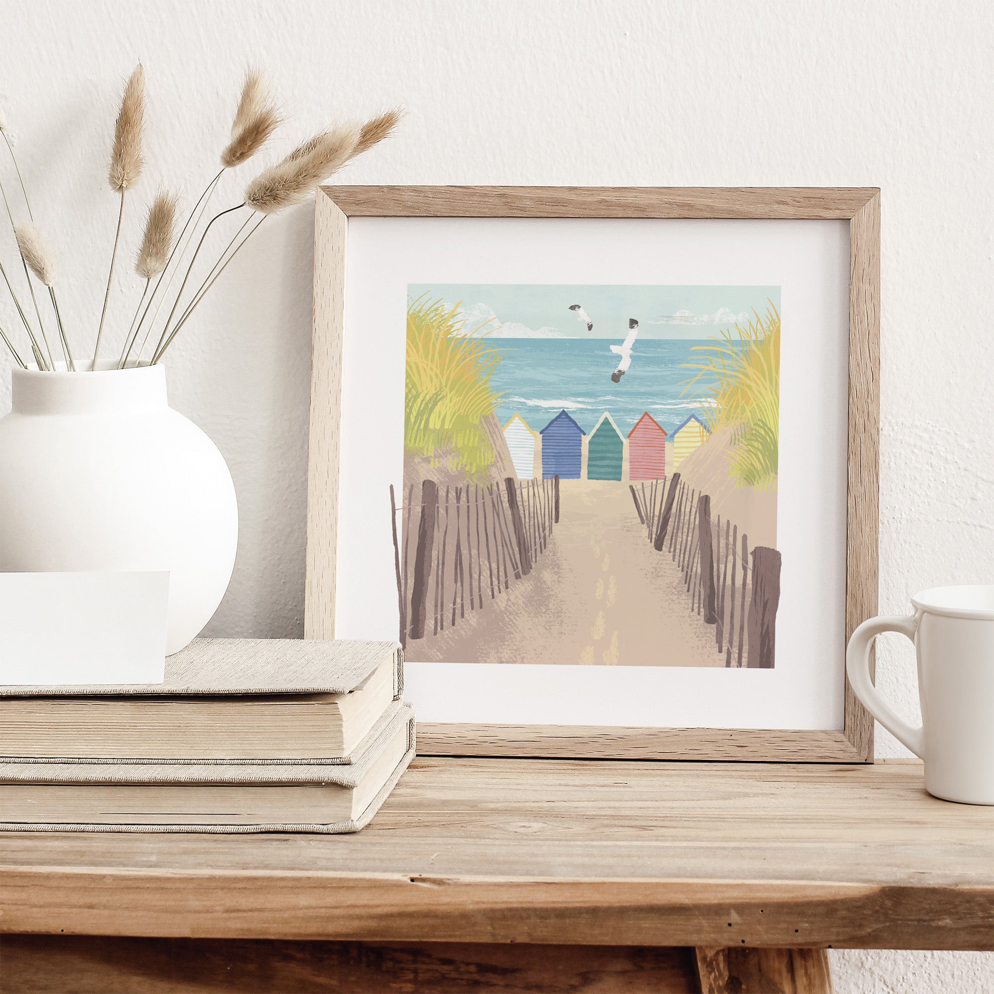 Framed artwork of beach huts on a wooden shelf with decor items.