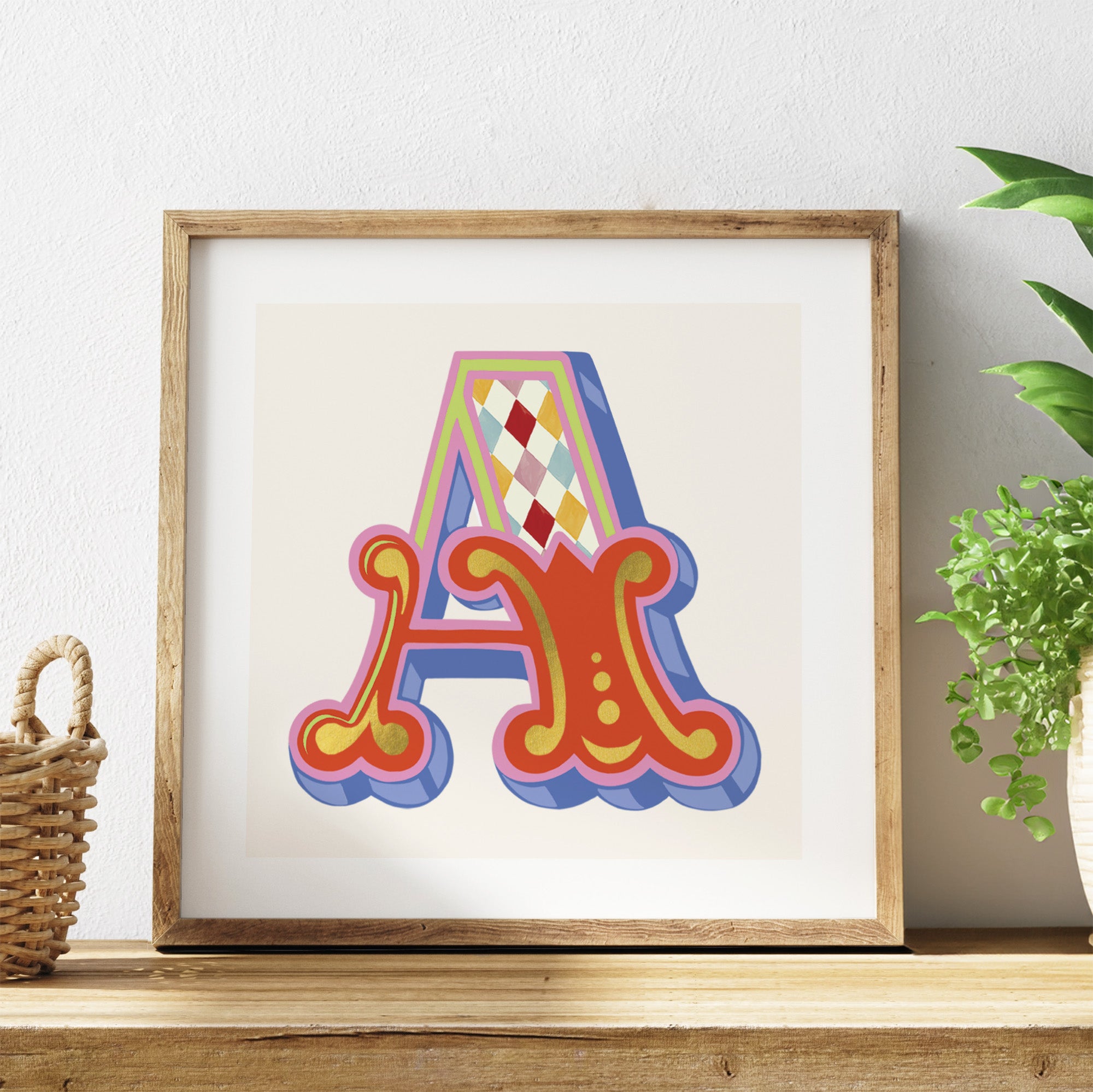 Framed colourful letter 'A' artwork on a shelf with a plant in the background.