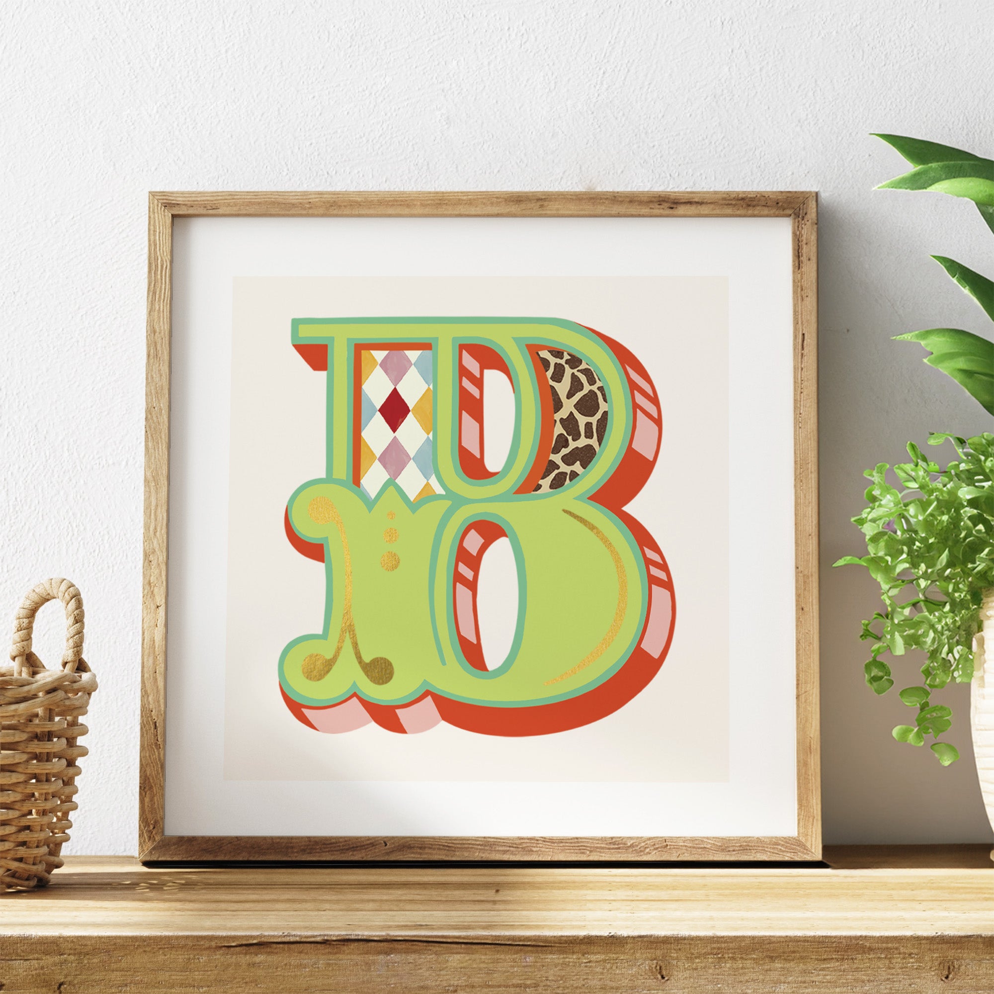 Framed colourful letter 'B' artwork on a shelf with a plant in the background.