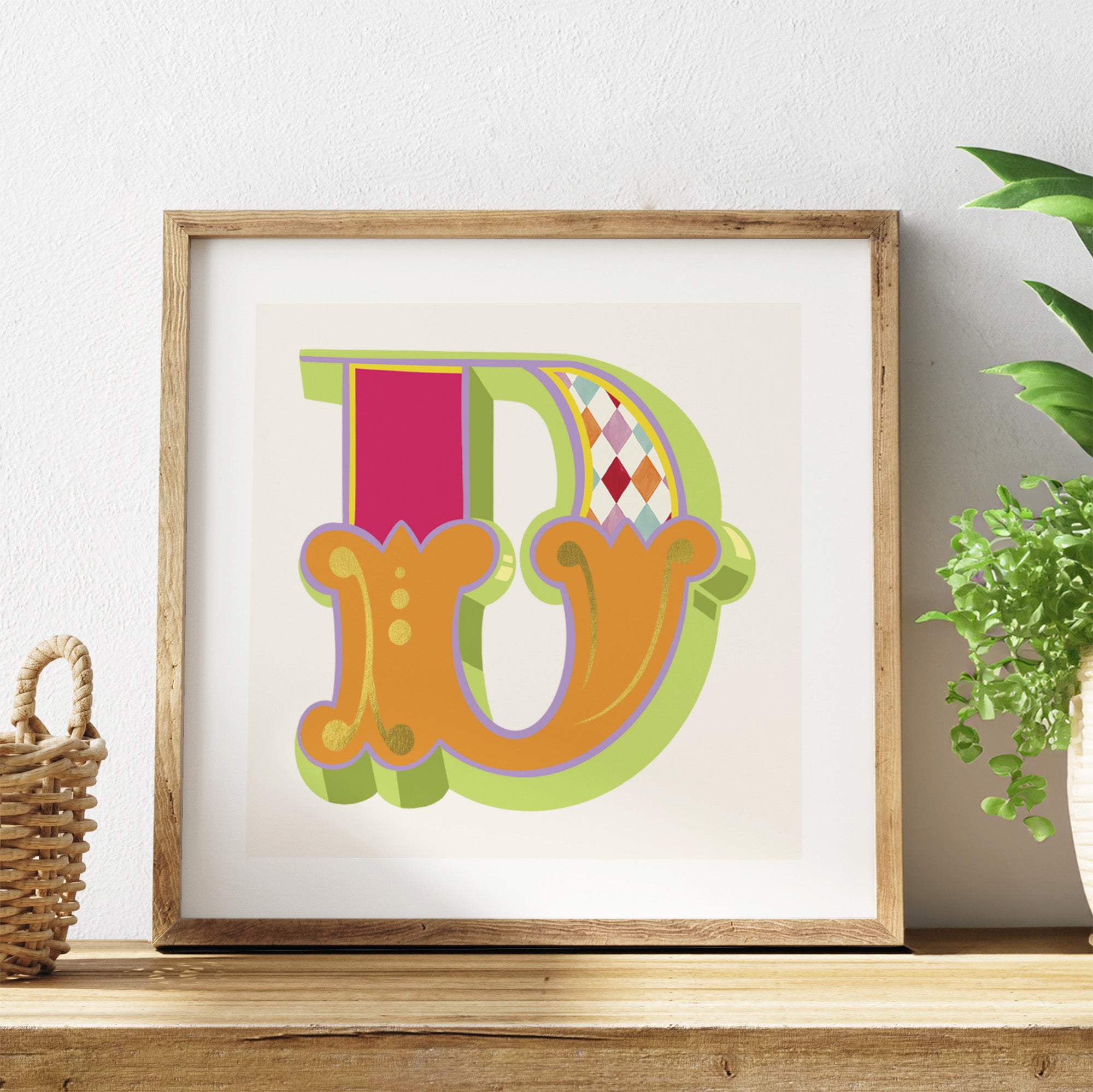Framed colorful letter 'D' on a white background with a plant and basket in the background.