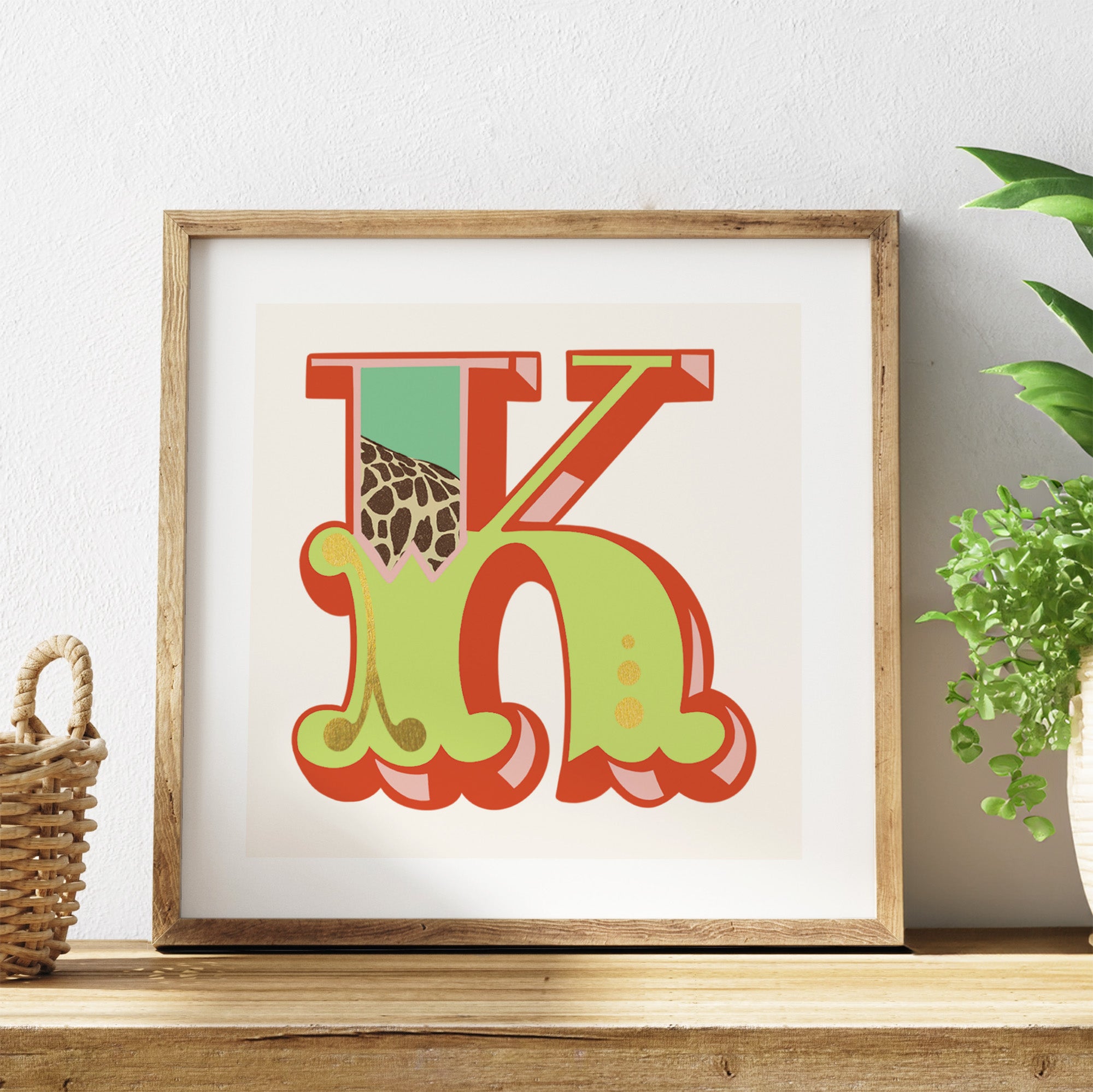 Framed artwork with colourful letter 'K' on a white background, placed on a wooden surface.