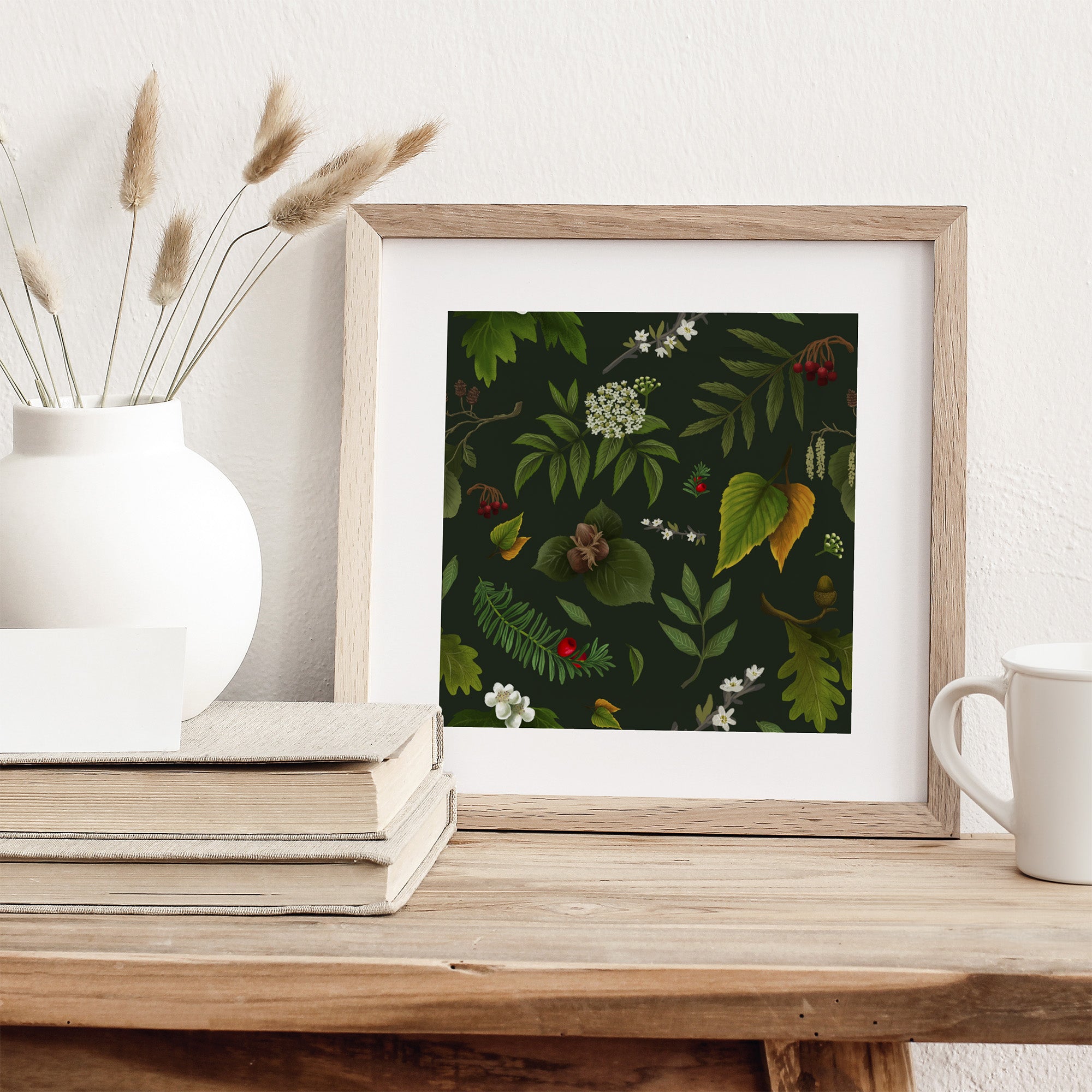 Framed art print featuring tree flowers and fruits on a green background. Print is leaning against a wall on a table.
