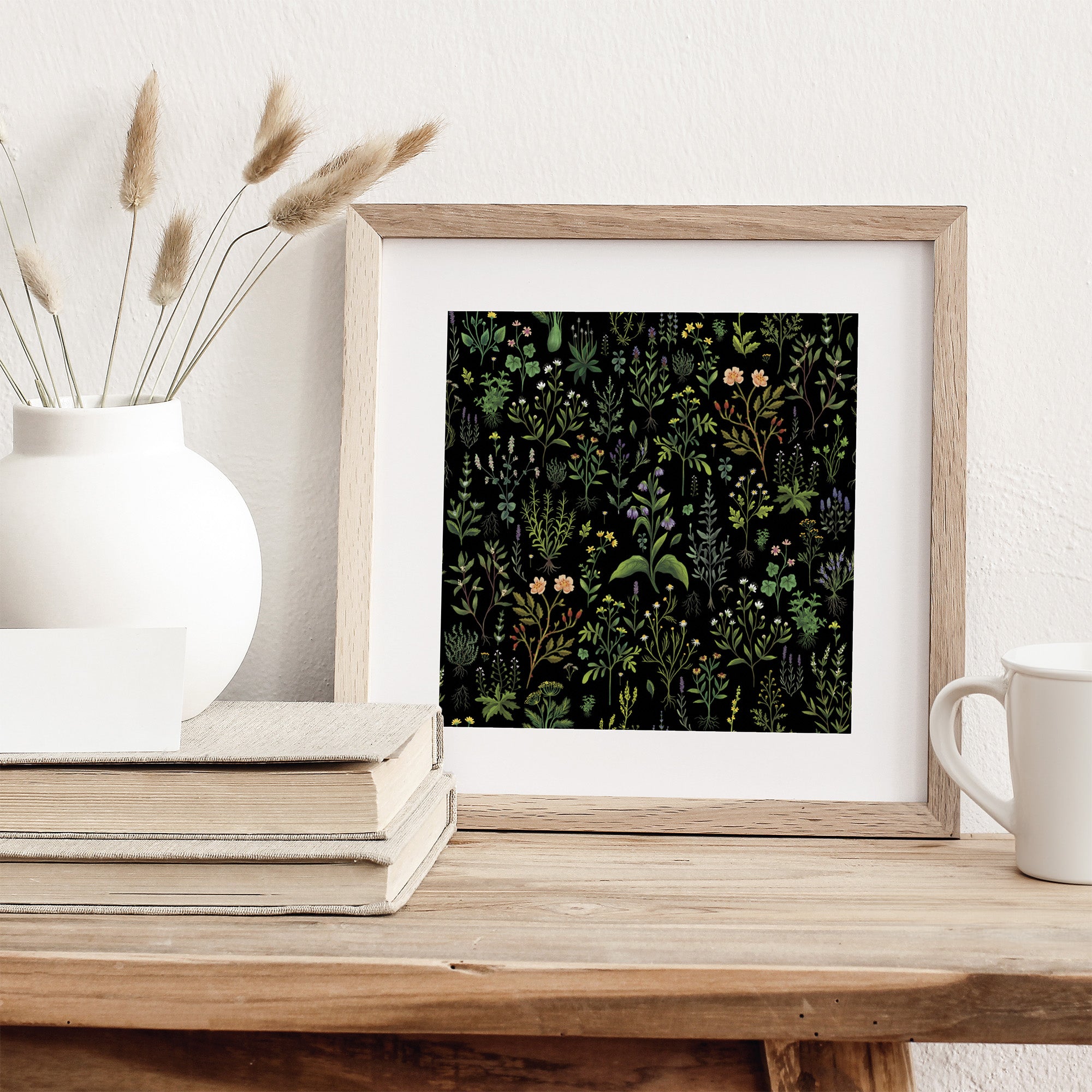 Framed art print featuring a herbal plant pattern on a black background. Print is leaning against a wall on a table.